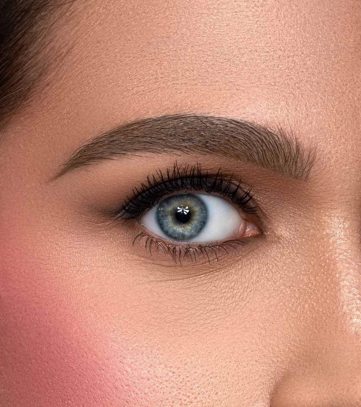 Primo piano di un occhio blu con mascara e fard sulla guancia.