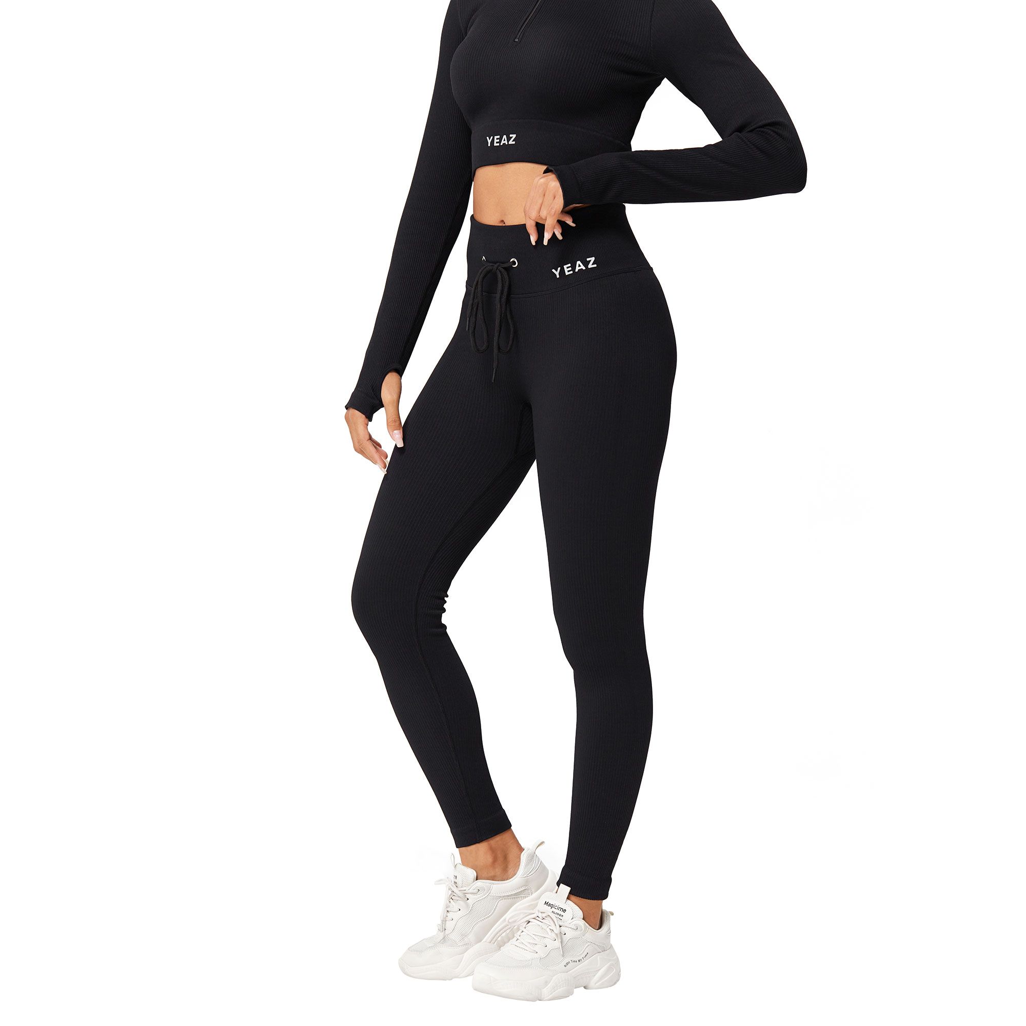 Completo sportivo nero a coste: crop top a maniche lunghe con fori per i pollici e leggings con coulisse. Marchio 'YEAZ' visibile.