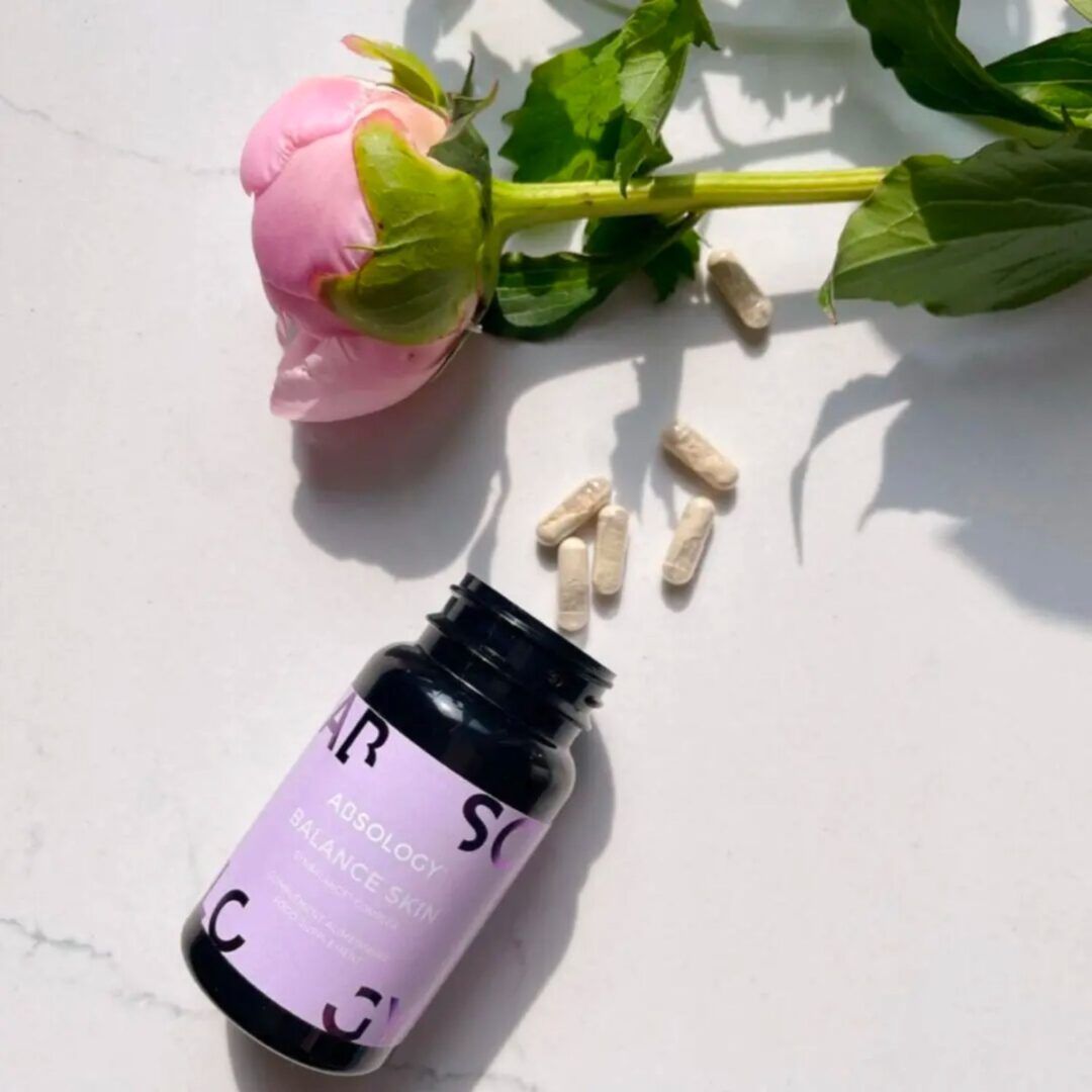 Flacone Absology Balance Skin e capsule. Fiore e stelo rosa. Su superficie marmorea.