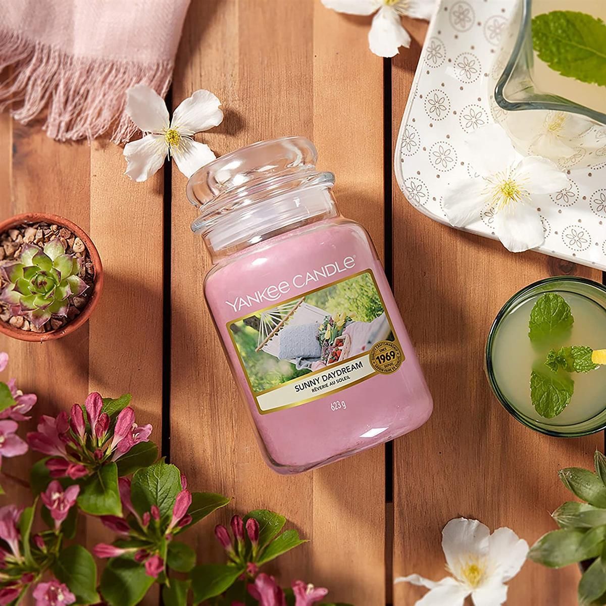 Candela profumata Yankee Candle Sunny Daydream. Candela rosa in barattolo di vetro. Etichetta con immagine amaca. Peso: 623 g. Su superficie in legno.