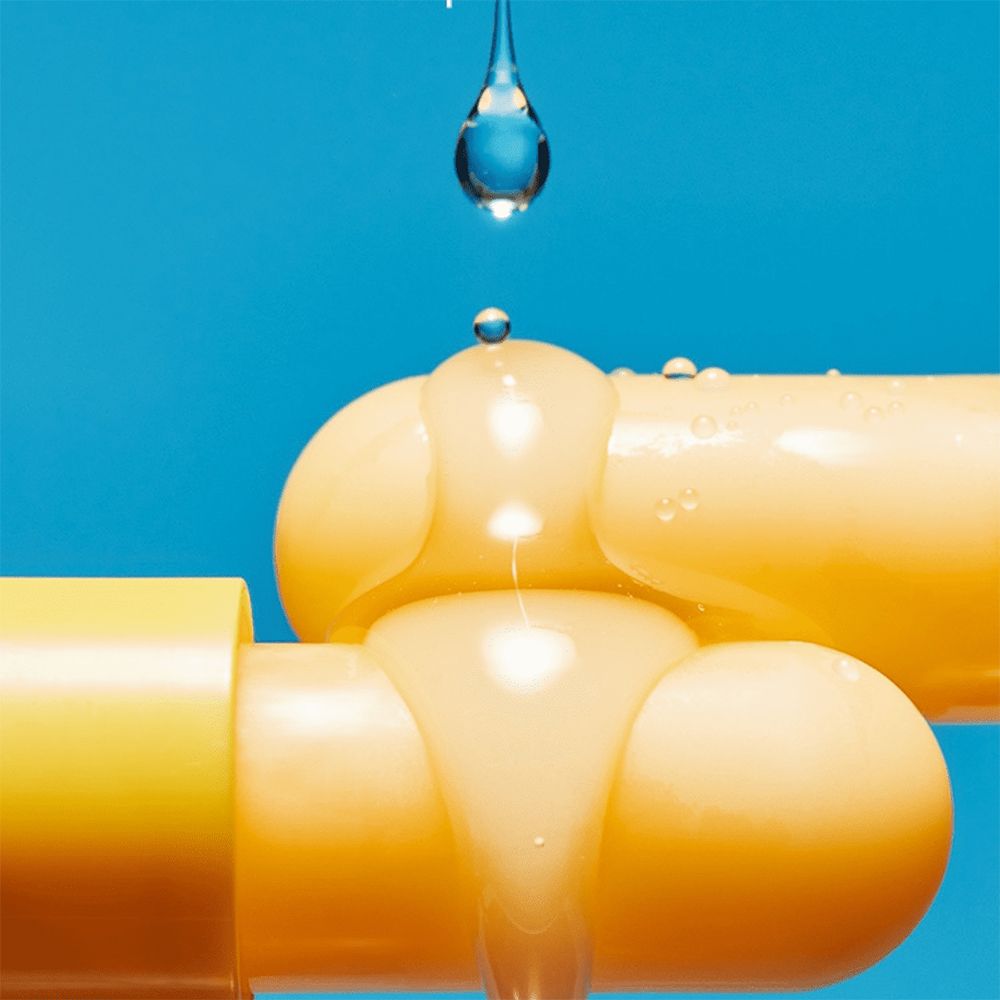 Balsamo per le labbra giallo, gocce di liquido. Il liquido gocciola sul balsamo. Sfondo blu.