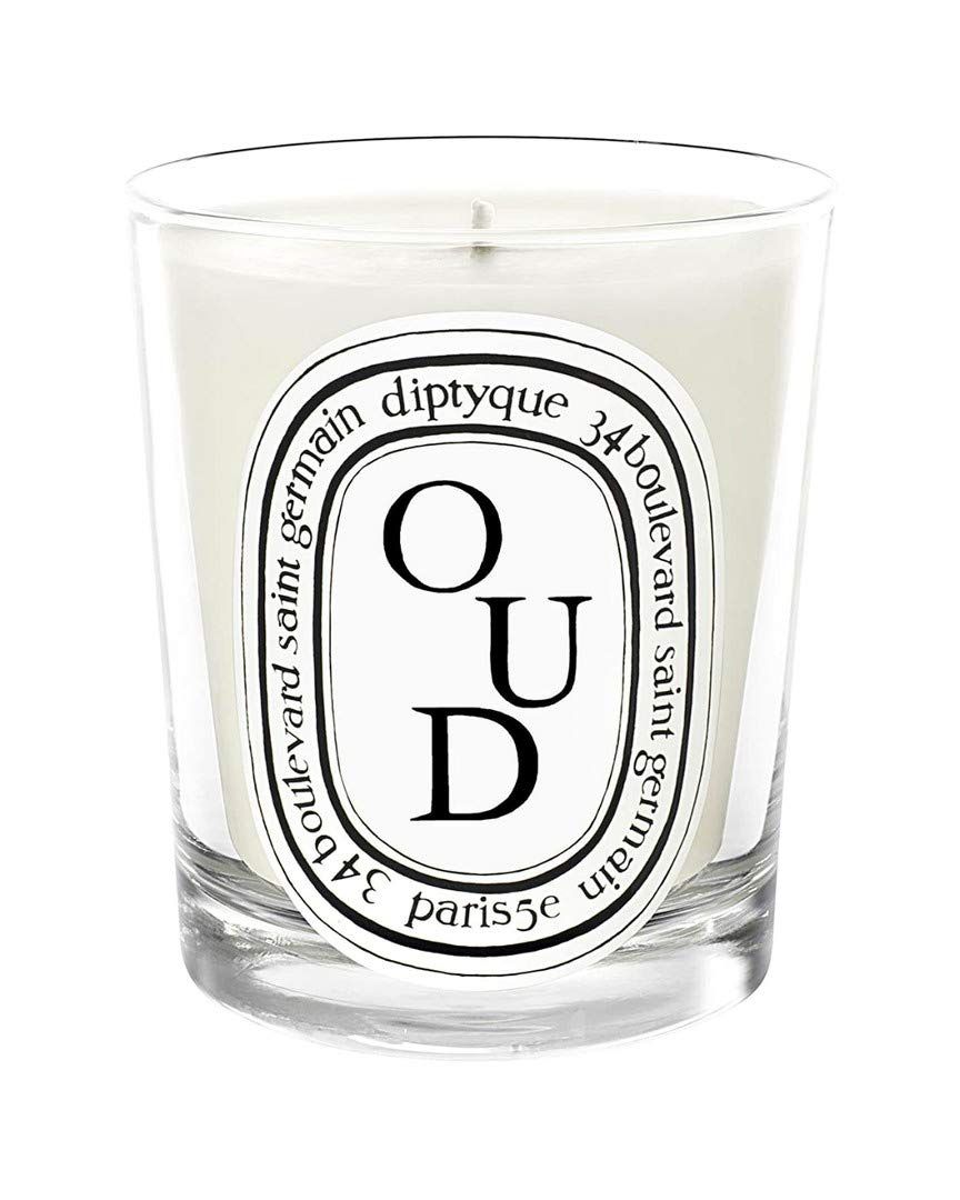 Candela in contenitore di vetro. Cera bianca, etichetta nera con testo: Oud, diptyque, 34 boulevard saint germain, paris 5e.