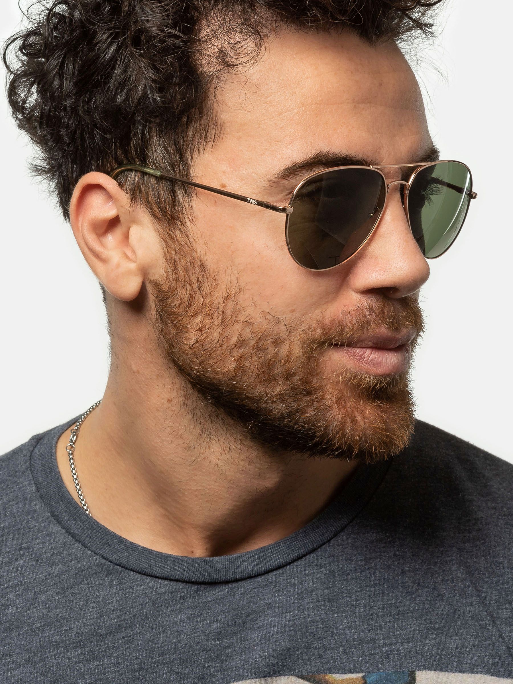 Uomo con occhiali da sole dorati e lenti verdi. Visibili barba e collana.
