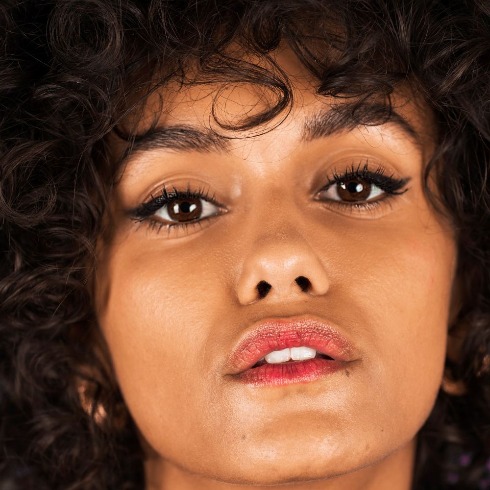 Ritratto di donna con pelle scura e ricci. Eyeliner nero sulle palpebre. Rossetto rosso.