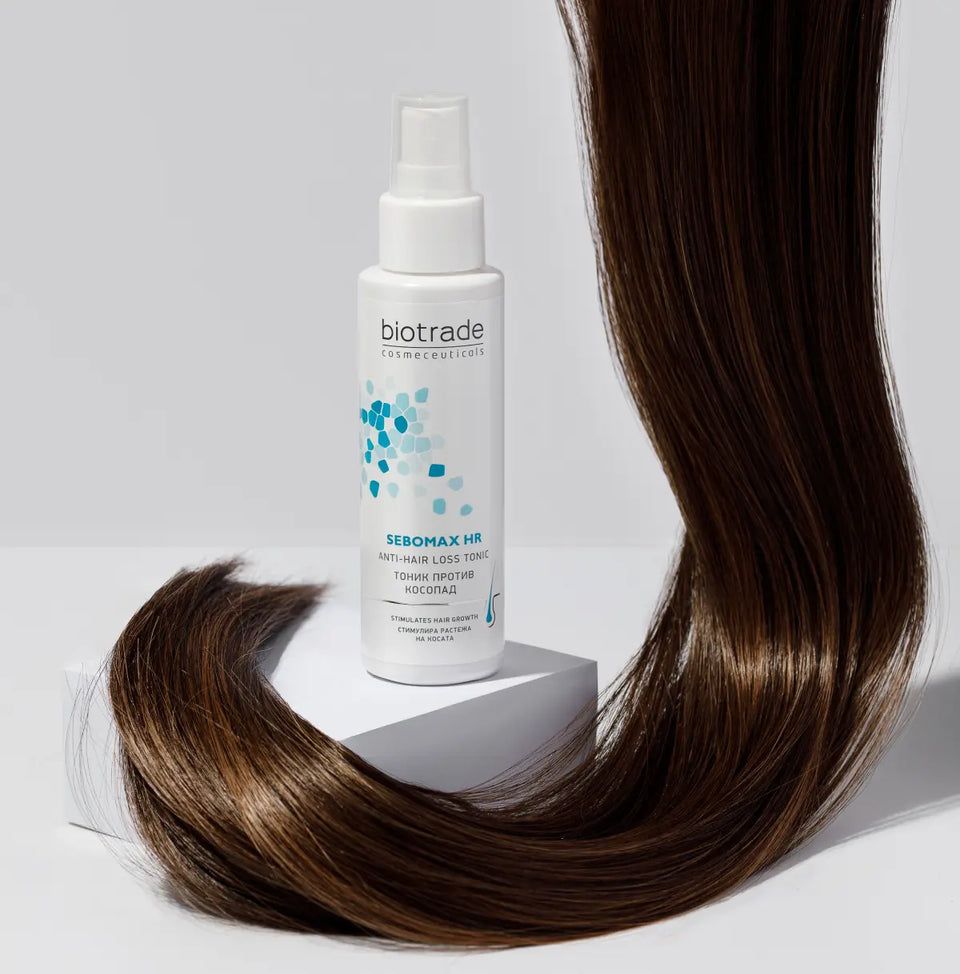 Flacone bianco con vaporizzatore. Logo Biotrade e nome del prodotto Sebomax HR. Ciocca di capelli accanto.