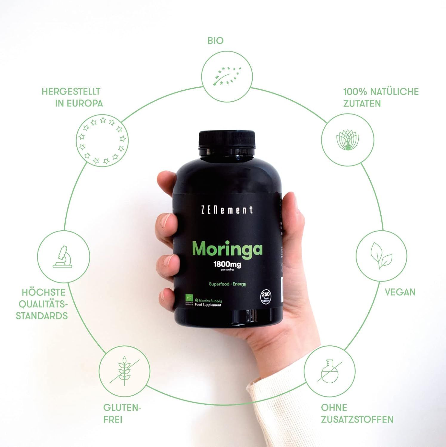 Flacone nero di capsule Zenement Moringa. Scritte: 1800mg, bio, vegano, senza glutine, senza additivi. Mano che tiene il flacone.