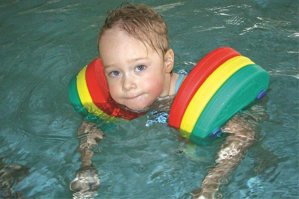 Un bambino in acqua con braccioli. I braccioli sono rossi, gialli e verdi.