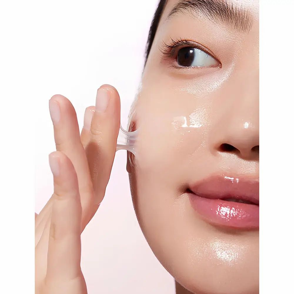 Primo piano di una donna che rimuove una sostanza trasparente dal suo viso. La pelle brilla.