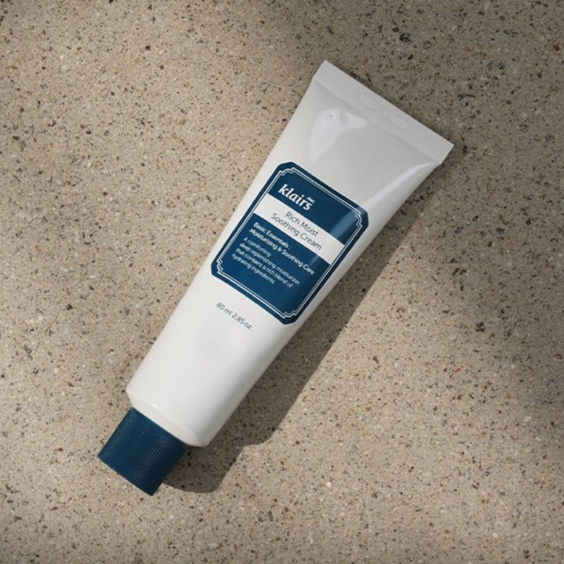 Tubo bianco con tappo blu. Scritta: klairs Rich Moist Soothing Cream. 80 ml. Su pietra.