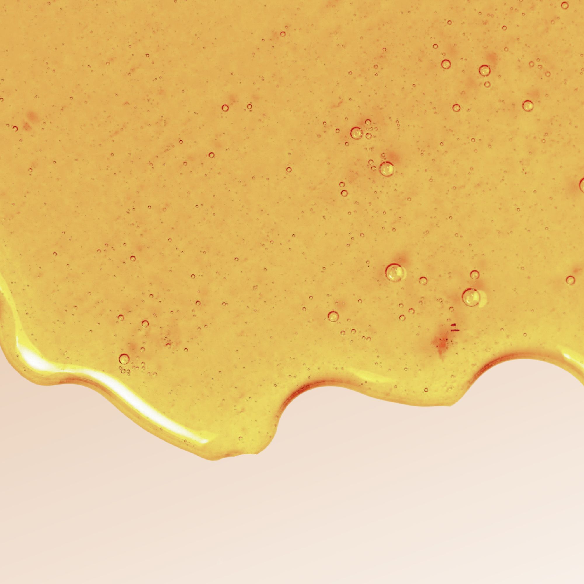 Liquido trasparente giallastro con bolle. Bordo ondulato. Su sfondo chiaro.
