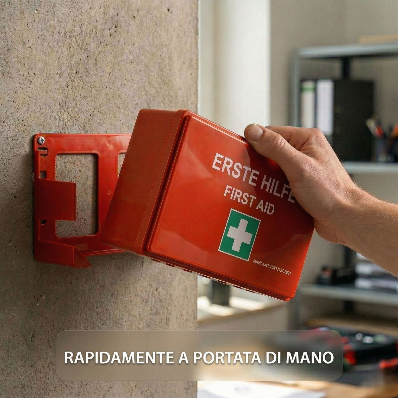 Cassetta di pronto soccorso rossa su supporto a muro. Scritta: Erste Hilfe/First Aid. Croce verde. Rapidamente a portata.