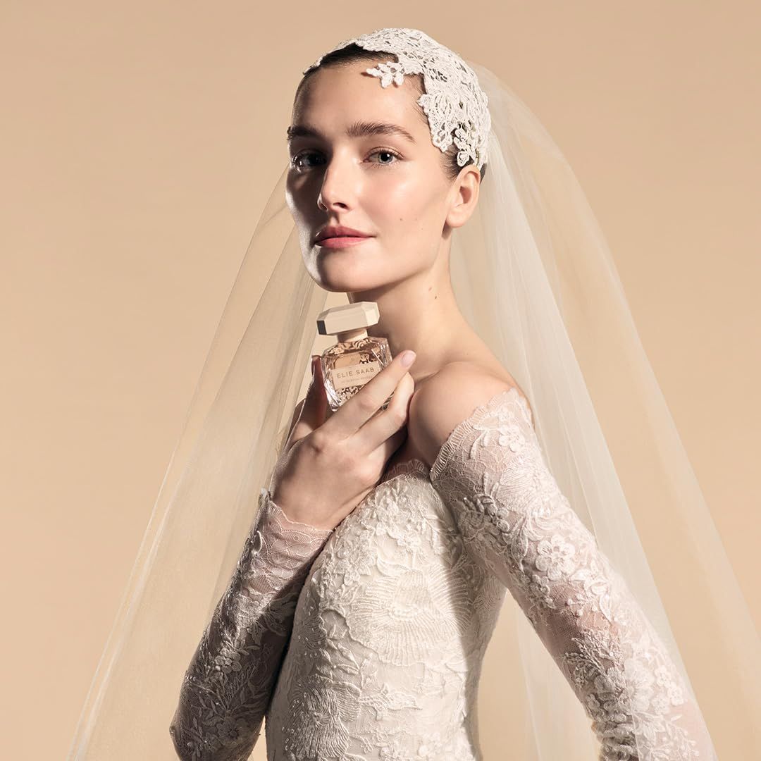 Sposa tiene flacone. Scritta: Elie Saab Le Parfum Bridal. Abito da sposa in pizzo, velo.