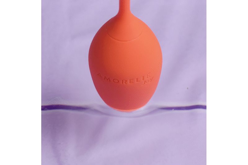 Oggetto arancione a forma di uovo con la scritta AMORELIE Joy. L'oggetto è immerso in un liquido.