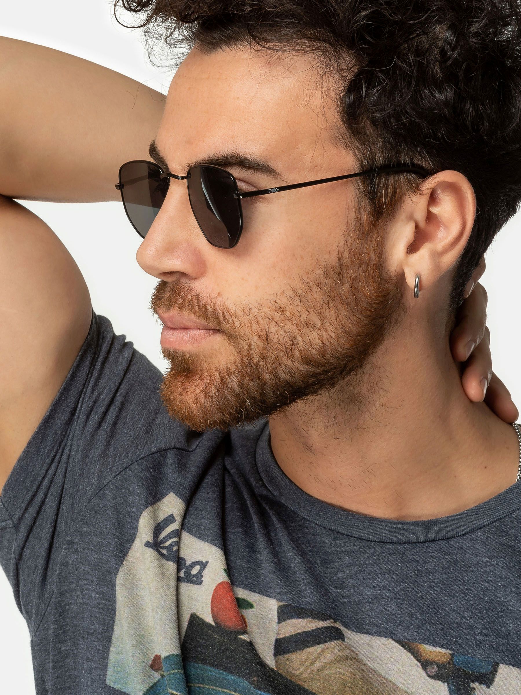 Uomo con occhiali da sole Twig, montatura nera, lenti esagonali.