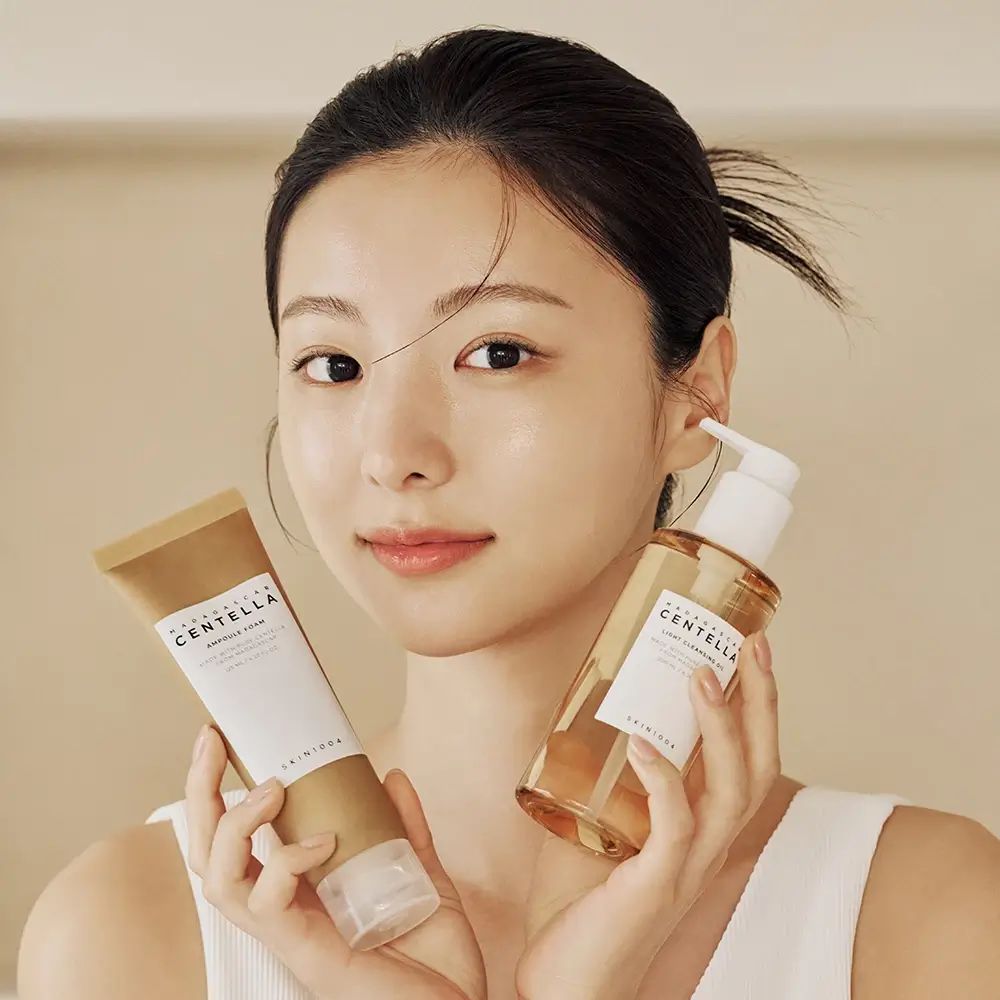 Una donna tiene in mano due prodotti. A sinistra, un tubetto, a destra, una bottiglia con pompa. Entrambi con etichette.