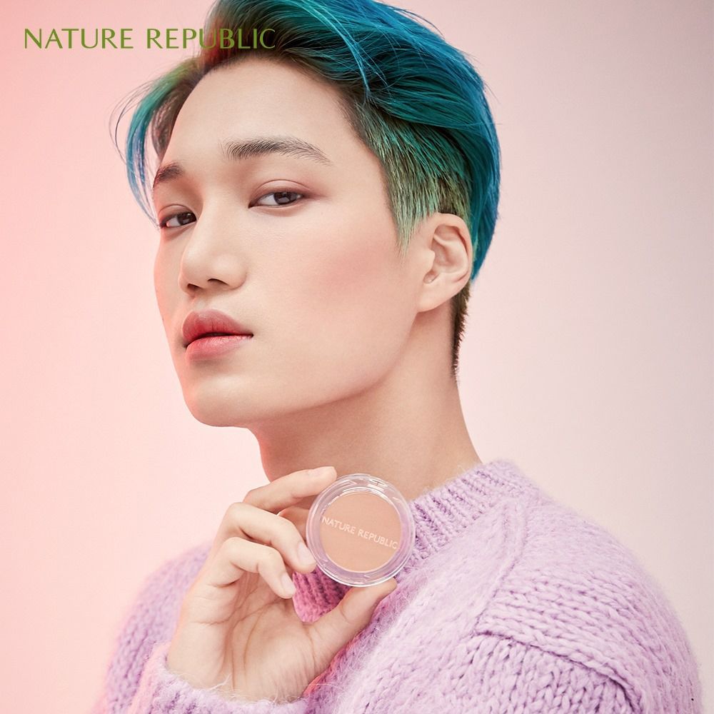 Persona tiene NATURE REPUBLIC By Flower Contouring Blush. Contenitore rotondo trasparente, contenuto rosa. Marchio visibile.