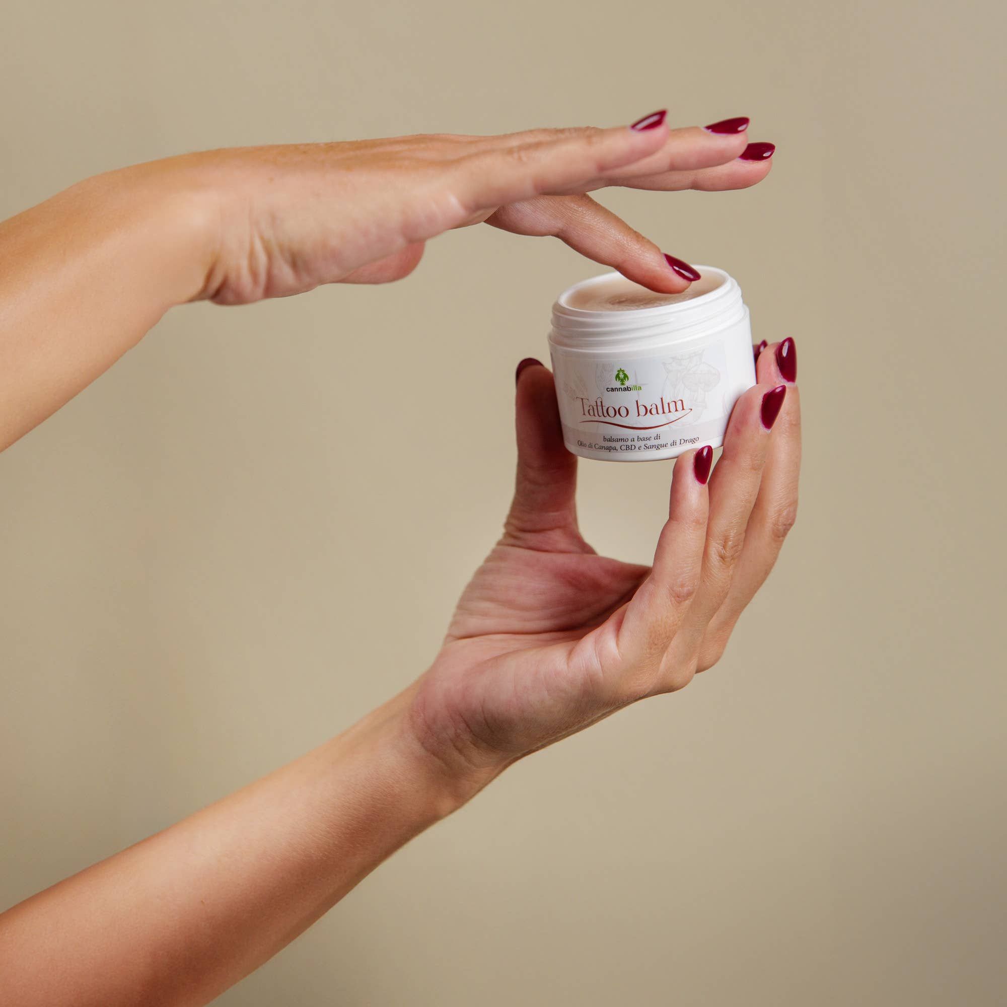 Le mani tengono un vasetto bianco con la scritta "Tattoo balm".
