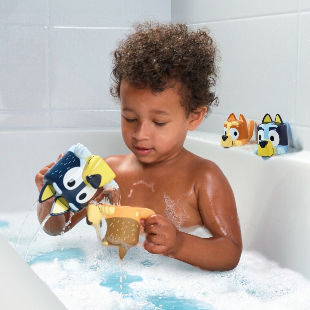 Bambino in vasca da bagno che gioca con giocattoli. L'acqua viene versata da un bicchiere. TOMY Bluey.