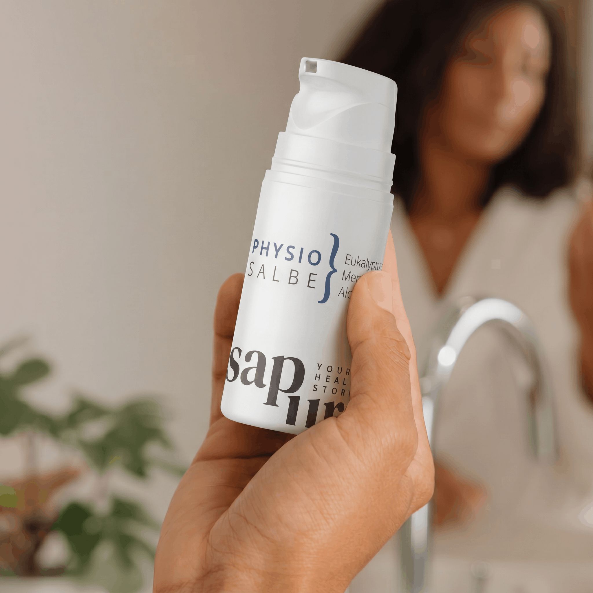 Mano che tiene un flacone bianco con erogatore a pompa. Etichetta: Physio Salbe, Eukalyptus, Menthol, Aloe Vera, sap pura.