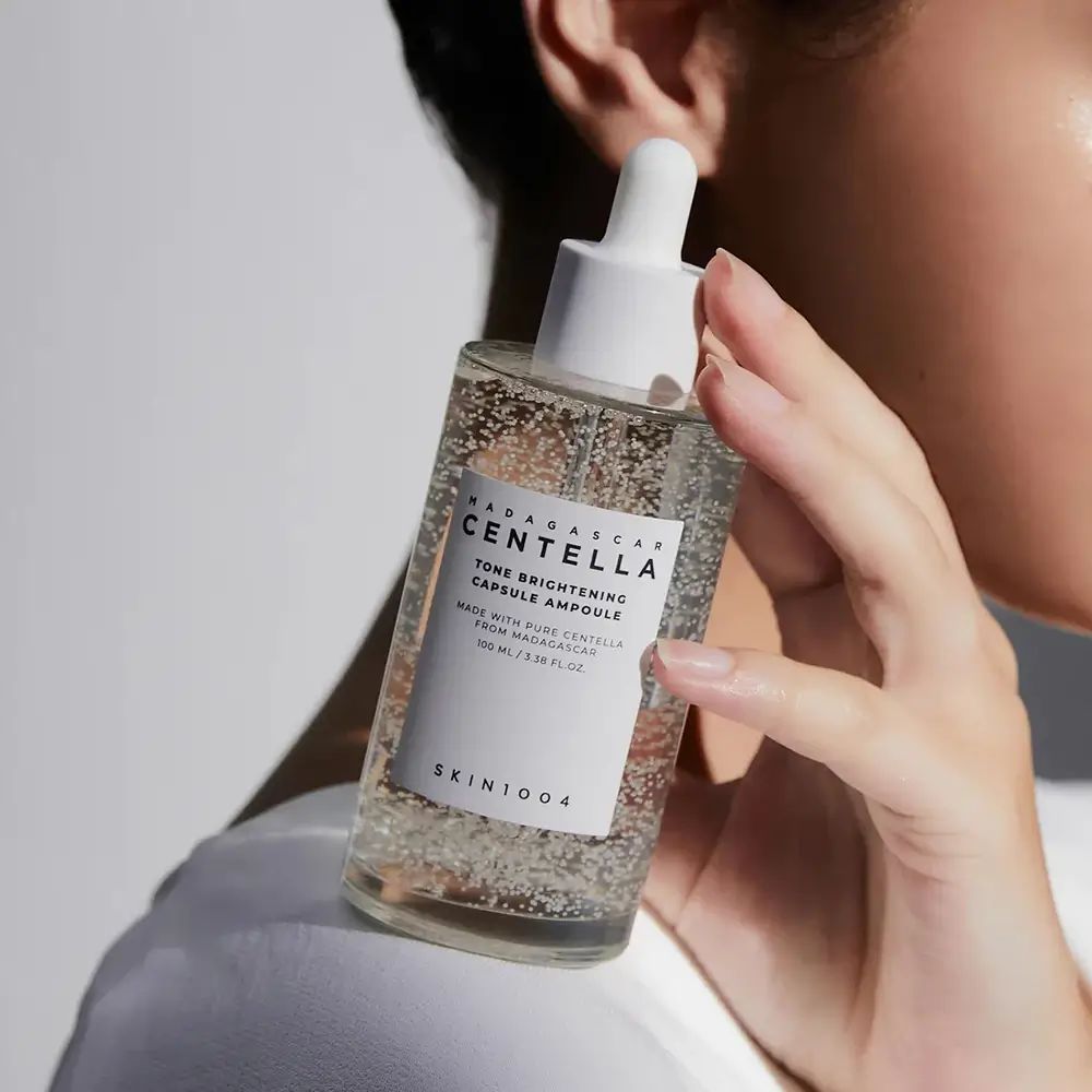Flacone di vetro trasparente con contagocce. Scritta: CENTELLA, TONE BRIGHTENING CAPSULE AMPOULE. Logo SKIN1004.