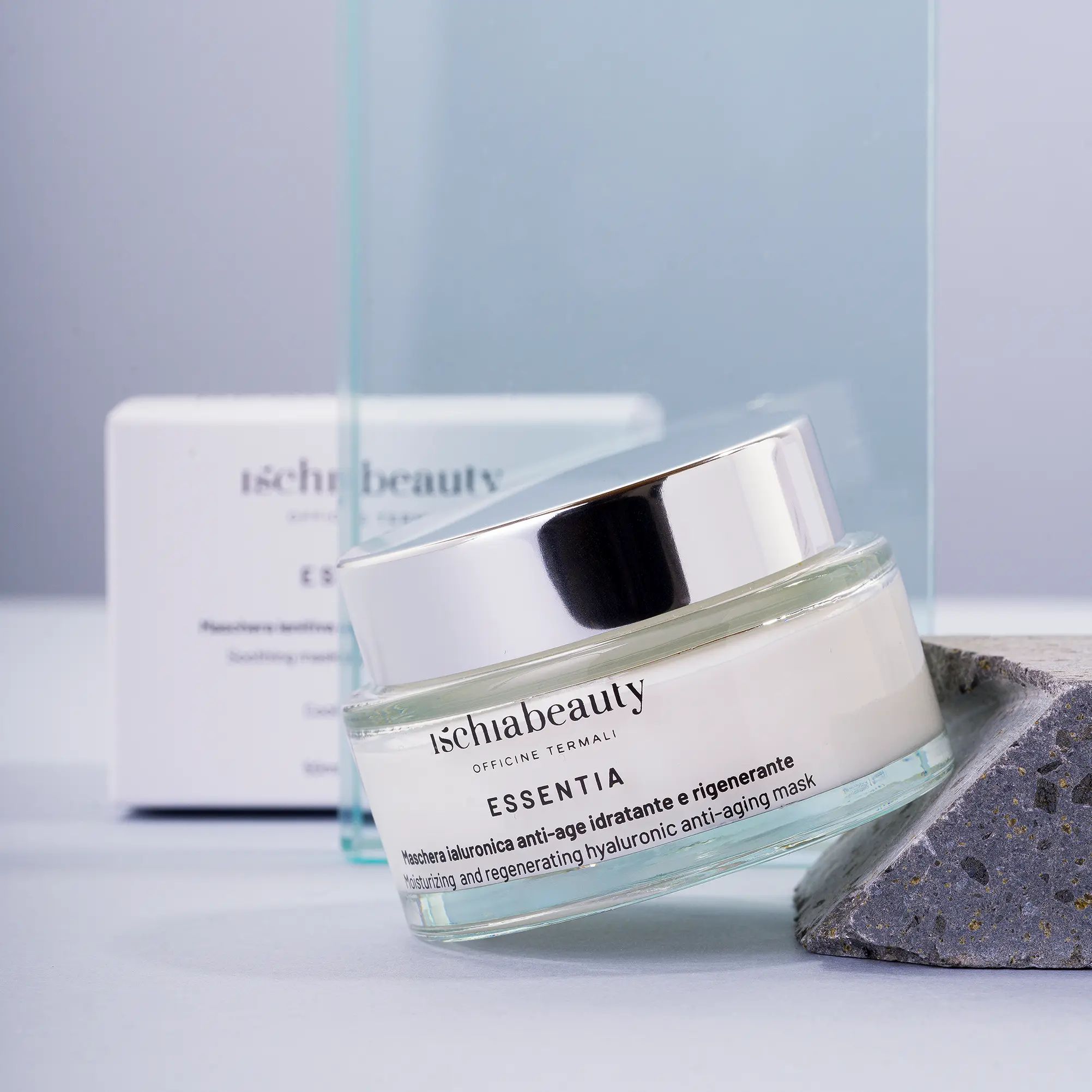 Vaso in vetro, coperchio argentato. Scritta: ischiabeauty ESSENTIA. Su pietra.