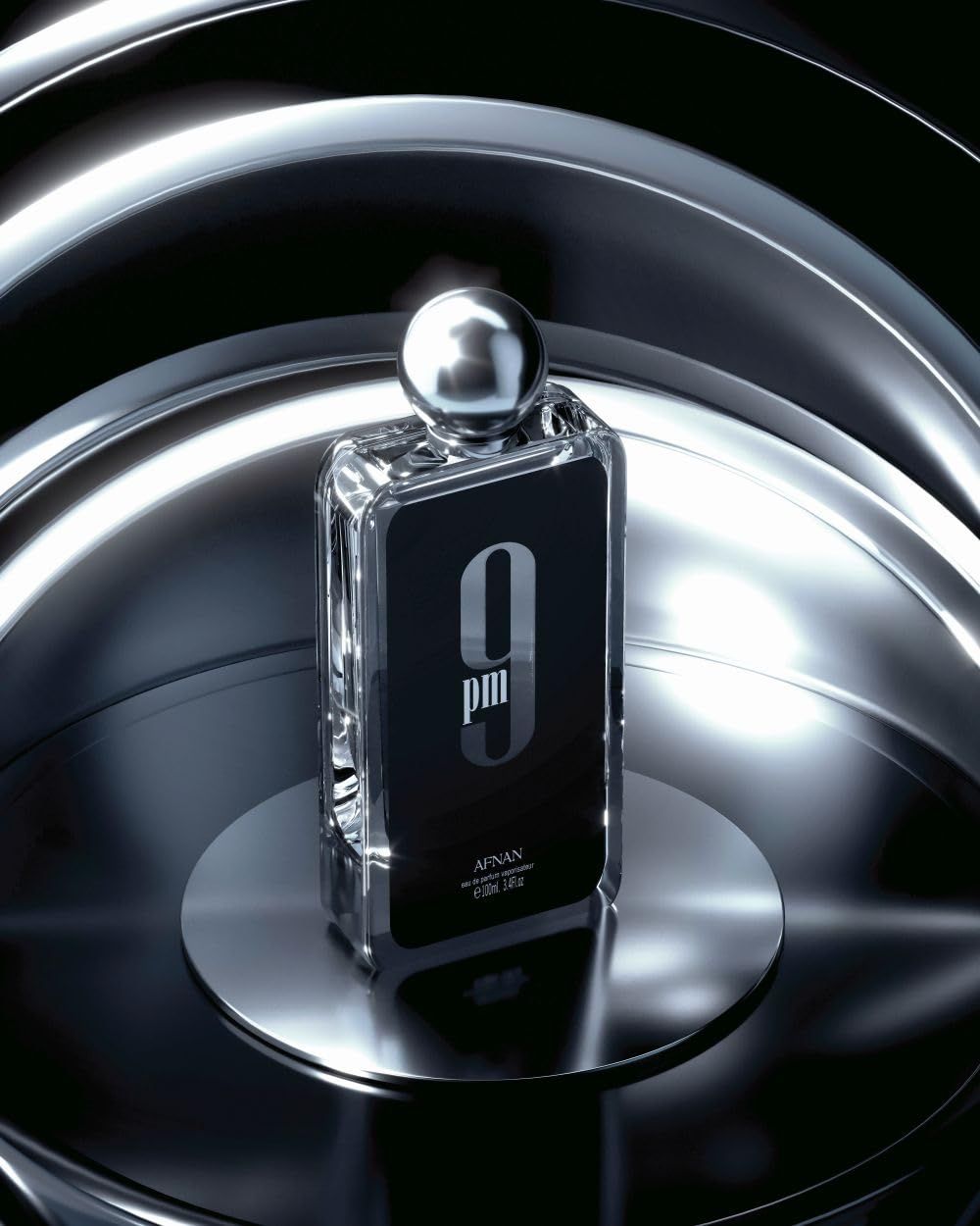 Flacone di profumo su una superficie metallica. Etichetta nera con scritta bianca '9 pm'. Tappo metallico.