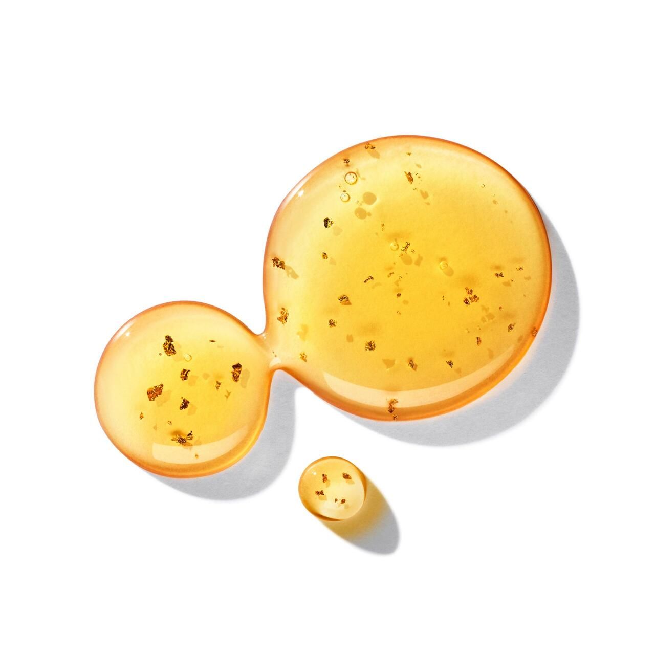 Gocce di liquido dorato con particelle dorate. Presentato su sfondo bianco.