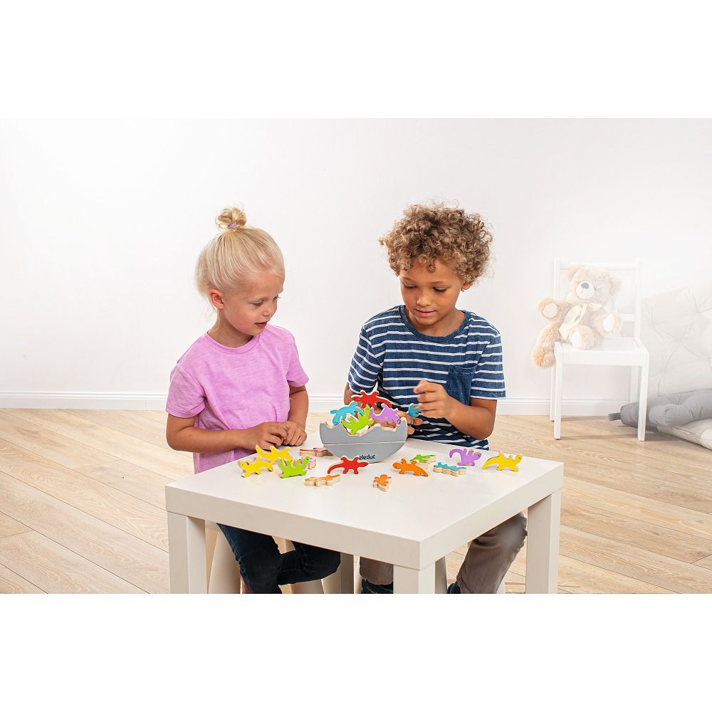 Due bambini giocano con lucertole di legno colorate su un tavolo. Una ciotola con lucertole.