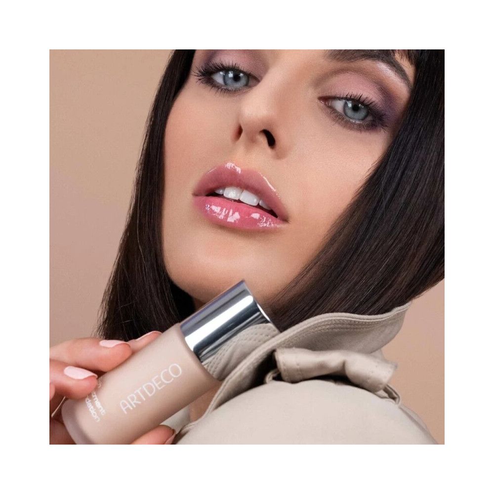 Donna tiene Artdeco Rich Treatment Foundation. Flacone con tappo argentato. Nome del prodotto e marchio visibili.