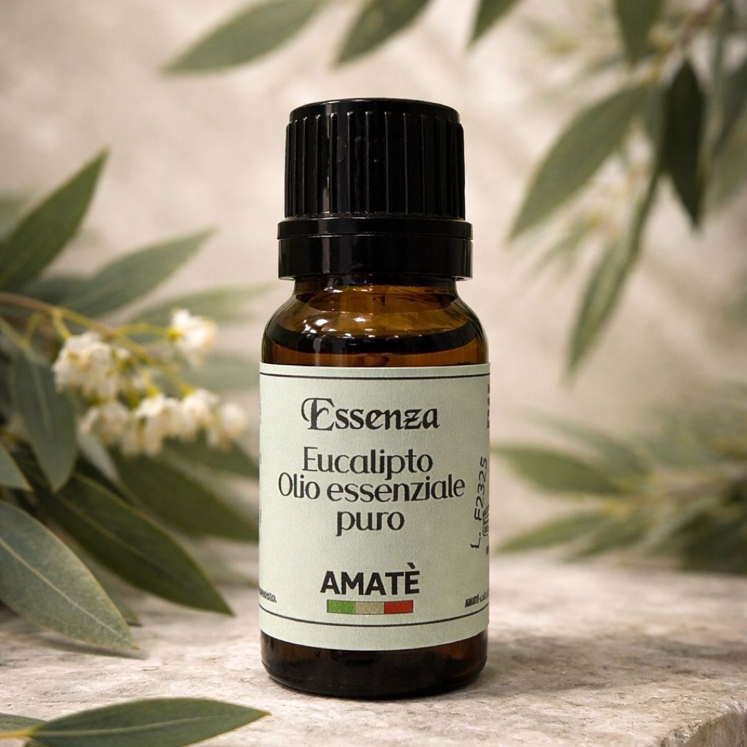 Flacone di vetro marrone con tappo nero. Etichetta con testo: Essenza Eucalipto Olio essenziale puro. Marchio: AMATÈ. Sfondo: foglie.