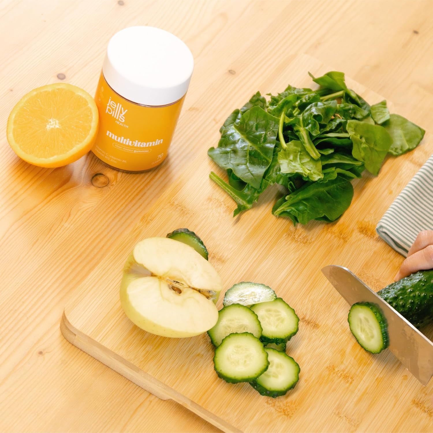 Un barattolo di Jelly Pills Multivitamin-Gummies, mezza arancia, spinaci, mela, cetriolo su un tagliere.