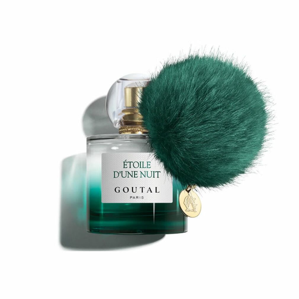 Flacone di profumo sfumato verde, tappo dorato e ciondolo. Un pompon verde è attaccato al flacone.