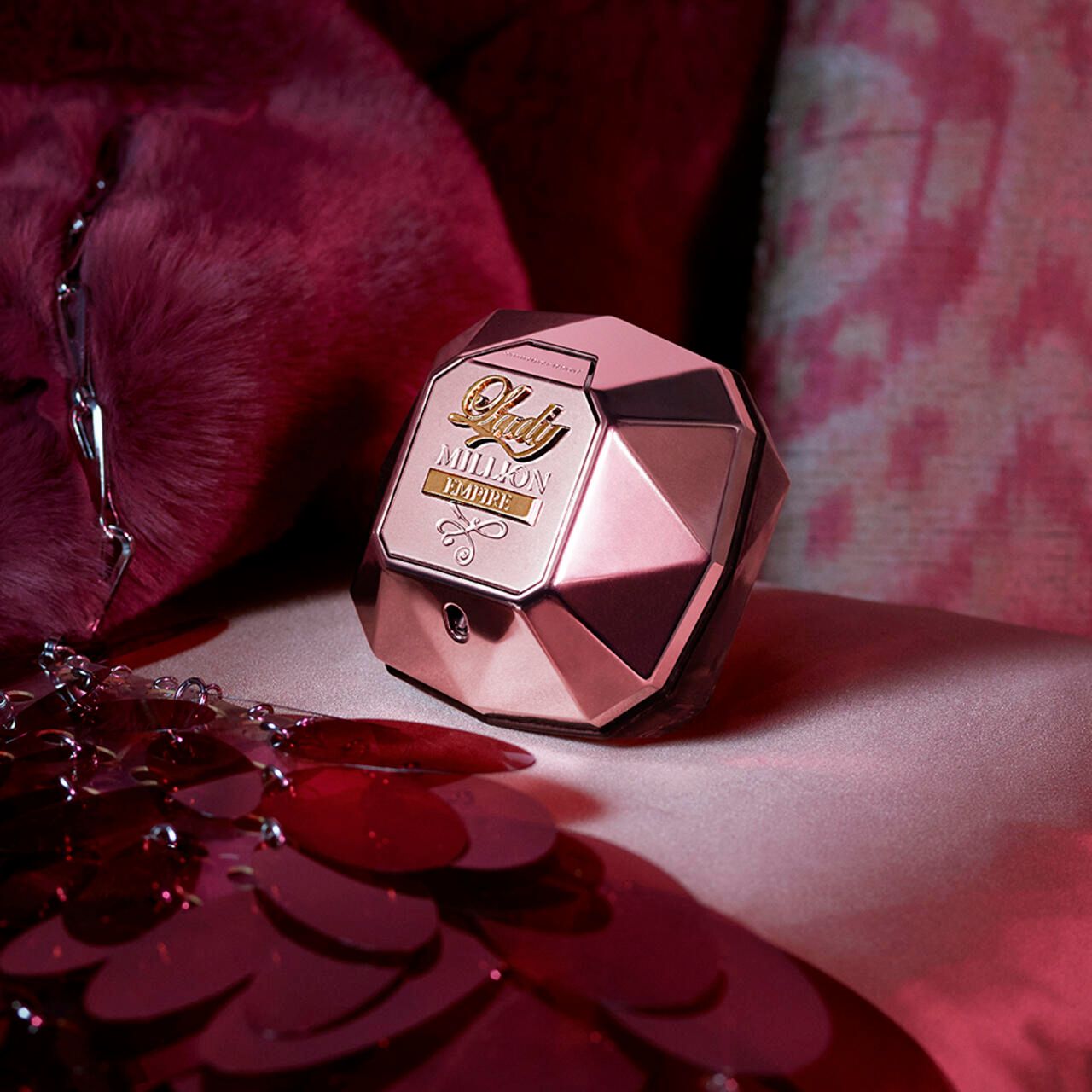 Flacone rosa con tappo dorato. Scritta: Lady Million Empire. Su sfondo rosso.