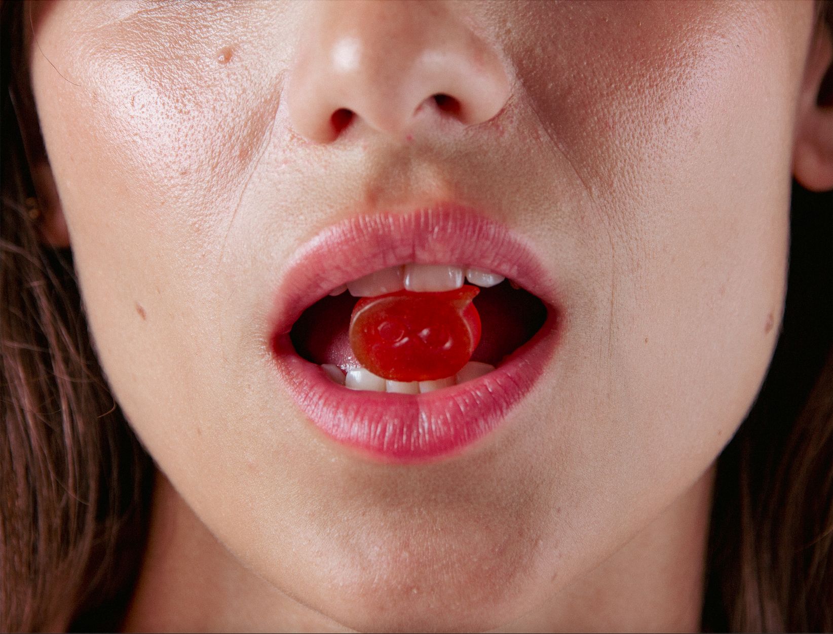 Primo piano di una bocca con una caramella gommosa rossa. Labbra e denti visibili.