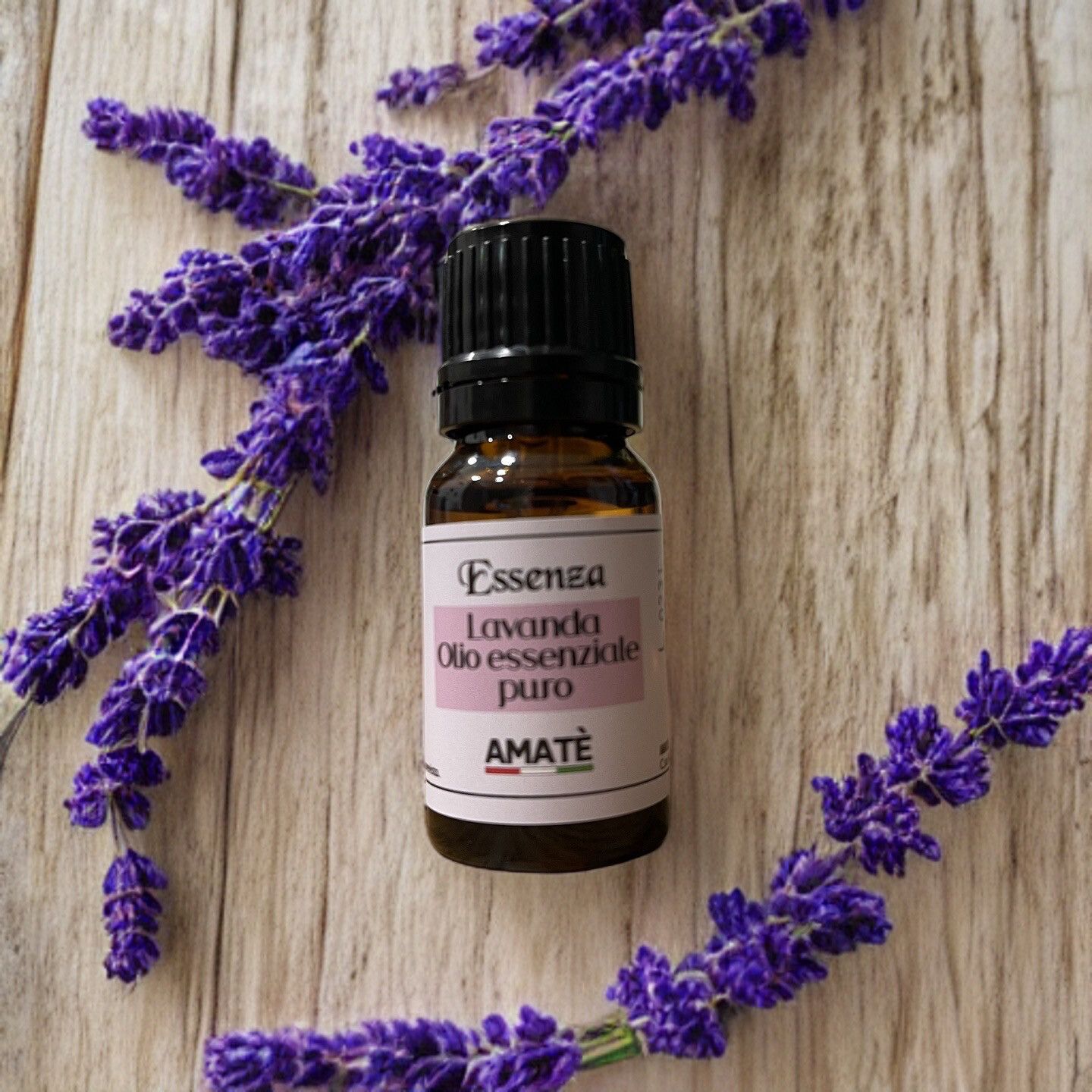 Flacone di vetro marrone con tappo nero, circondato da rametti di lavanda. Etichetta con testo: Essenza Lavanda Olio essenziale puro. Marchio: AMATÈ.