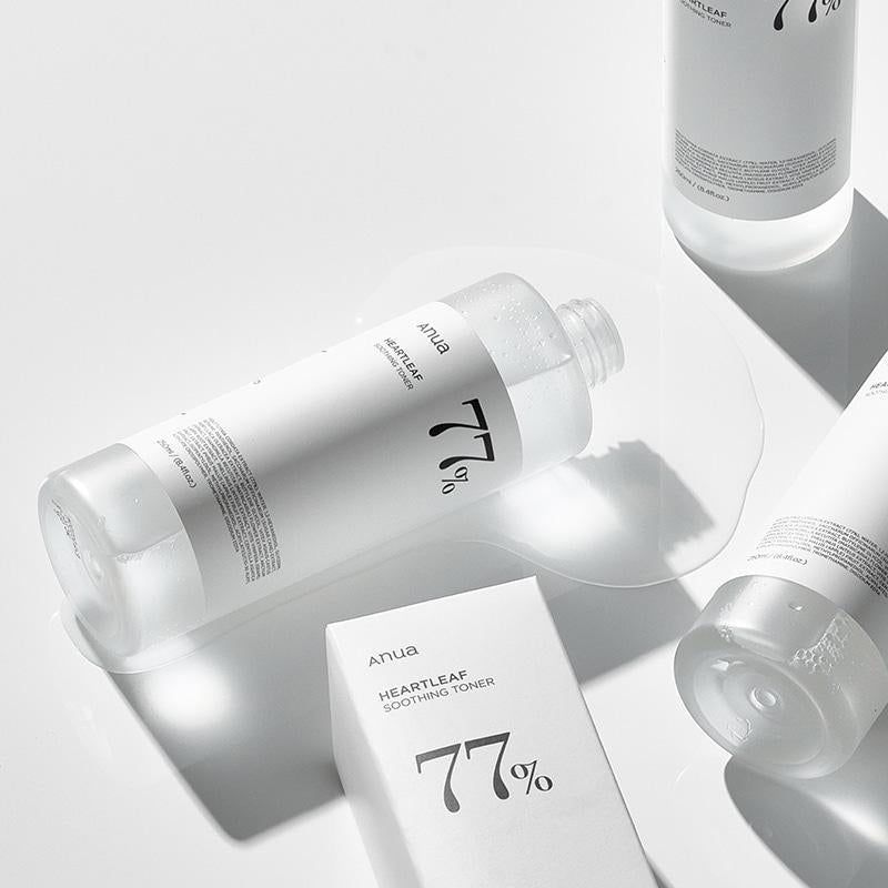 Diversi flaconi bianchi e una scatola. Scritte: Anua, 77%, Heartleaf Soothing Toner. Liquido sulla superficie.