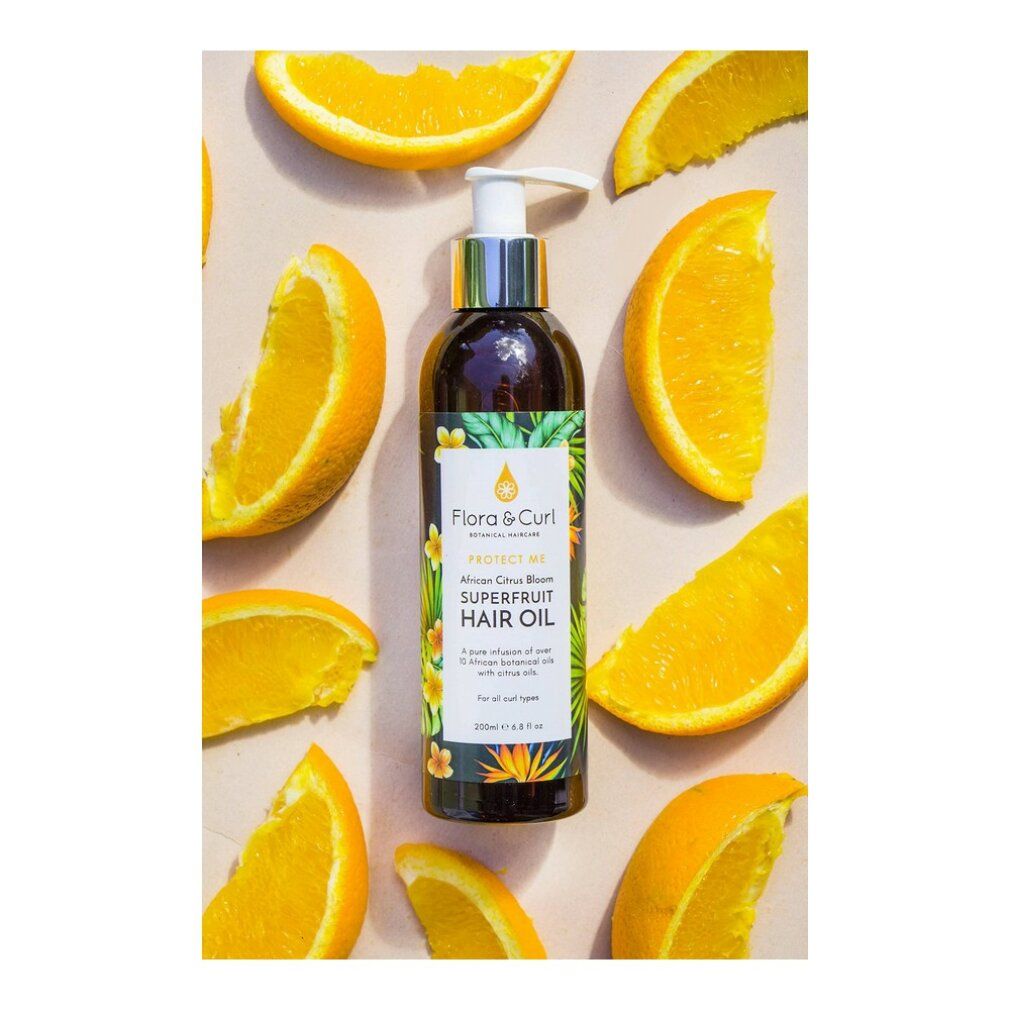 Flacone marrone con pompa, circondato da fette d'arancia. Etichetta con testo: Protect Me African Citrus Superfruit Hair Oil.