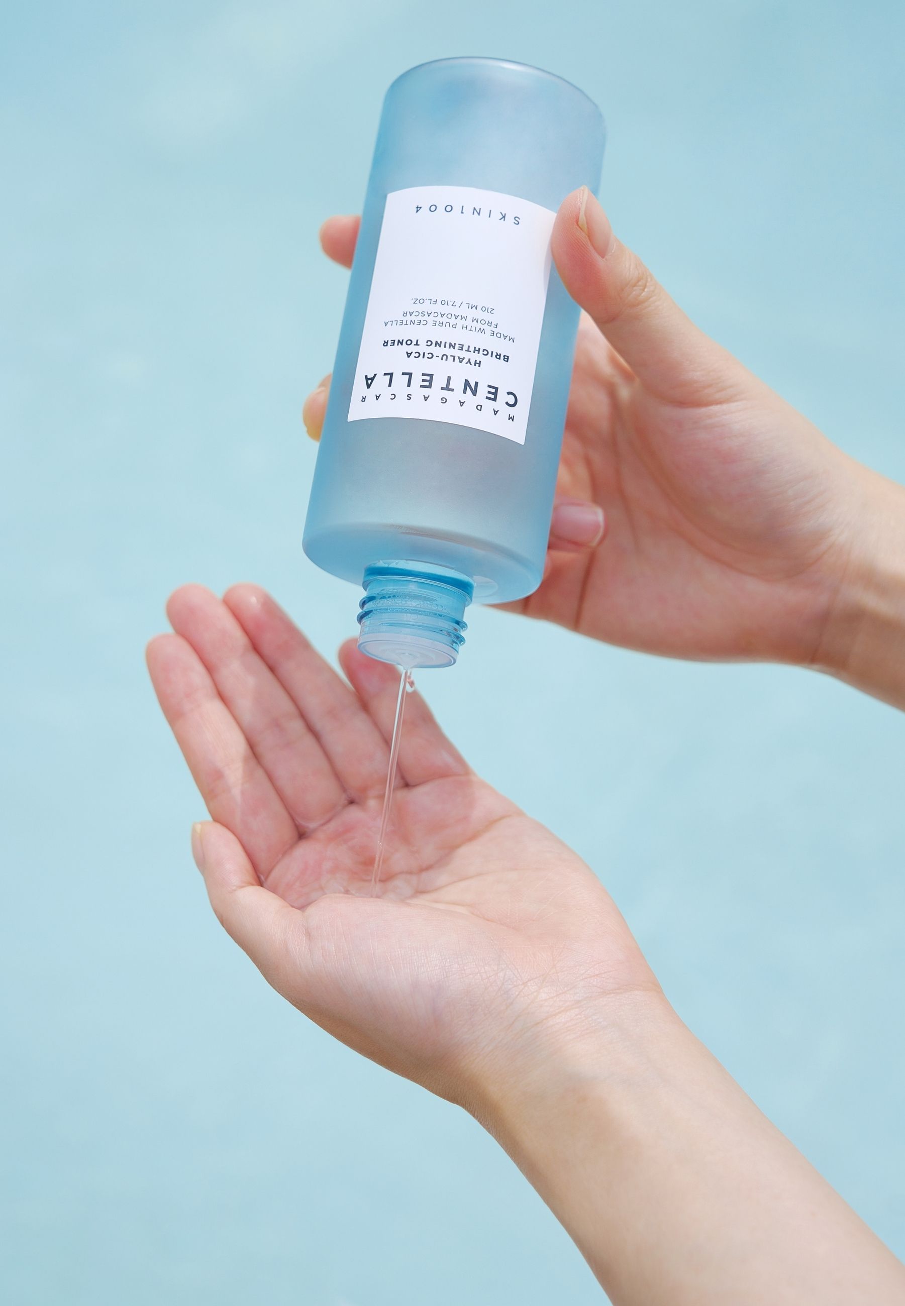 Mani che tengono una bottiglia da cui fuoriesce del liquido. Sfondo azzurro.