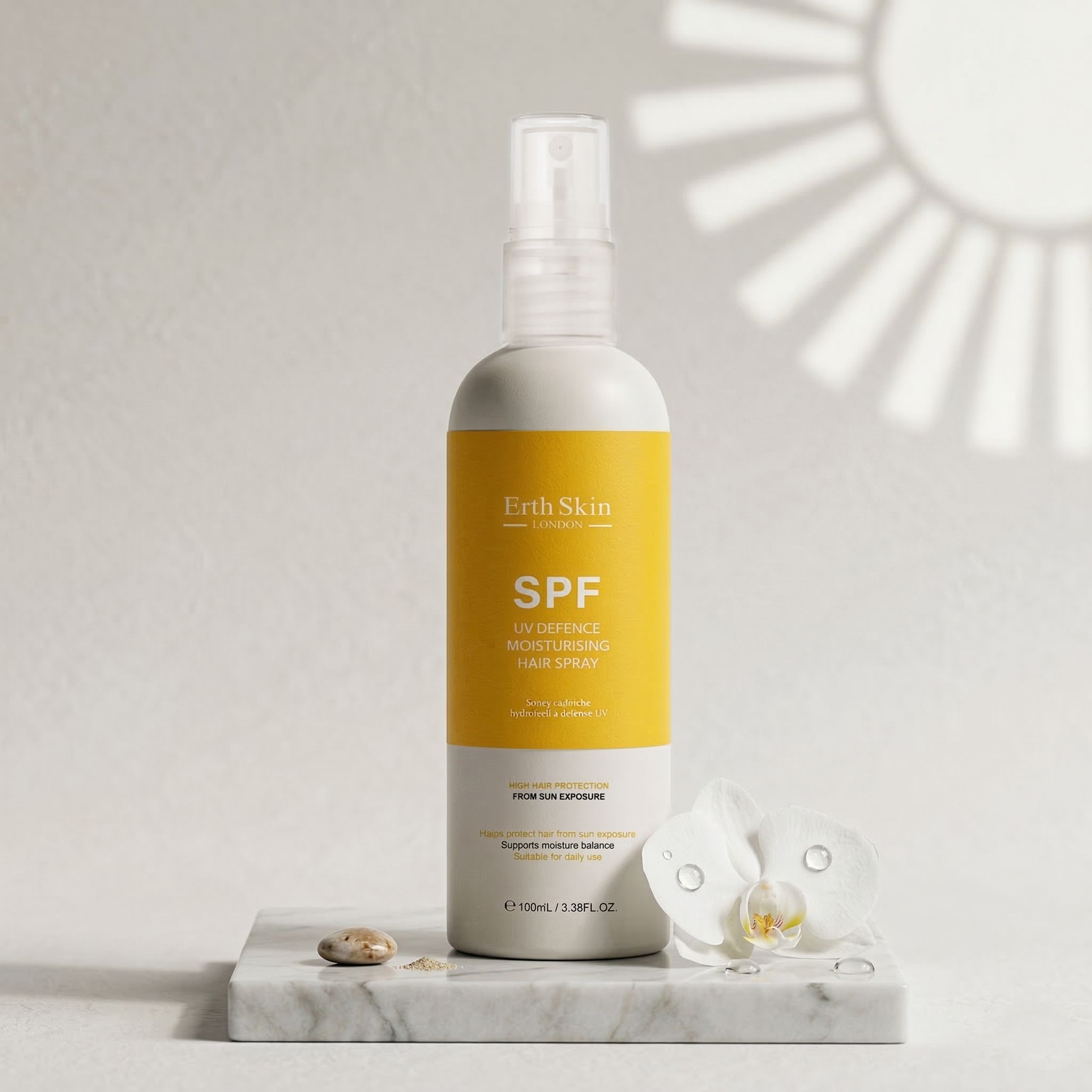 Flacone di spray per capelli con etichetta gialla. Scritta: SPF. ErthSkin London. Su lastra di marmo con fiore e pietra.