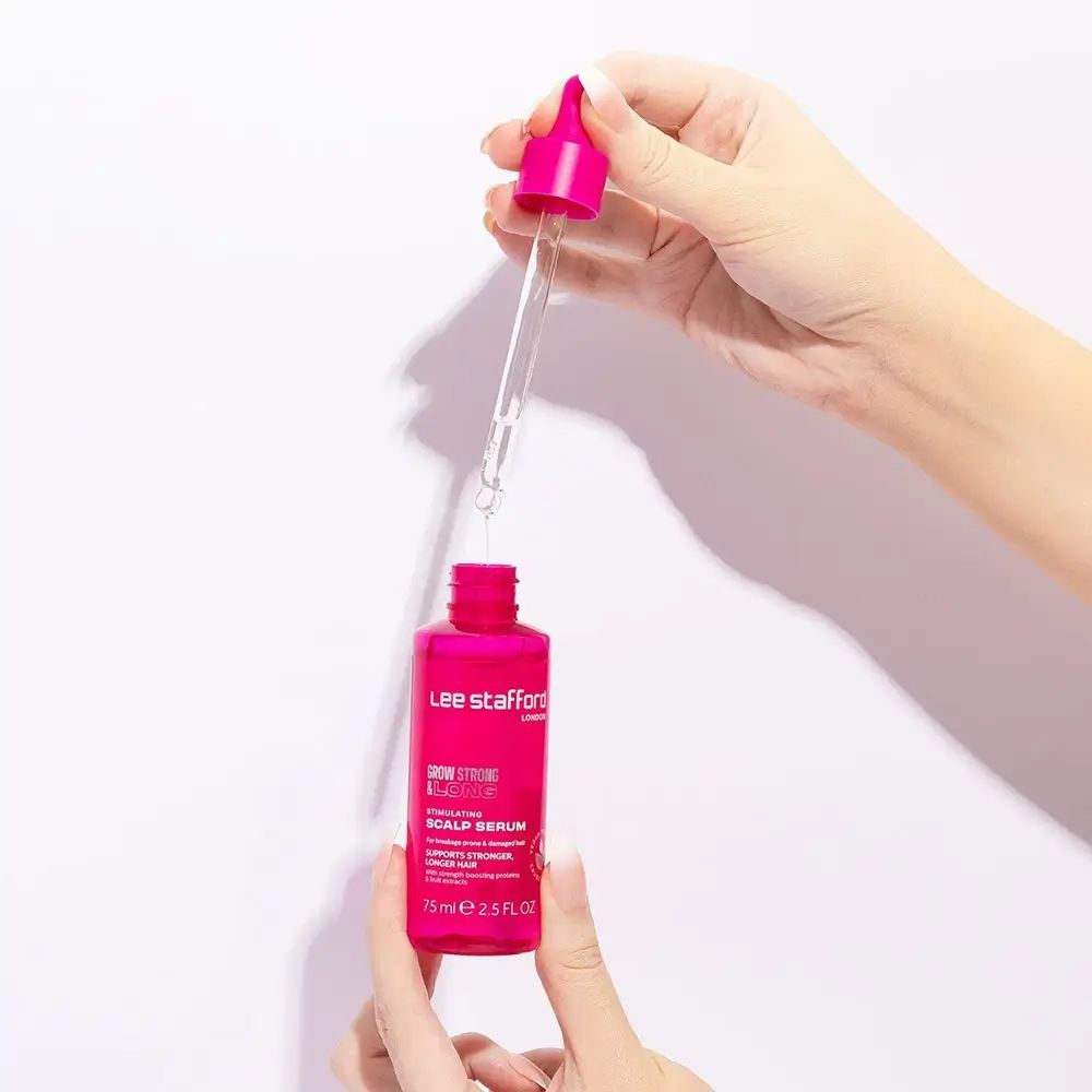 Mani che tengono un flacone contagocce rosa e una pipetta del siero Grow Strong & Long di Lee Stafford.