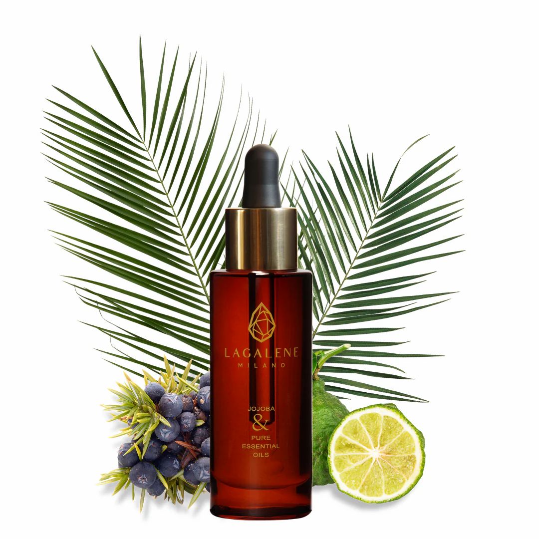 Flacone di vetro marrone di Lagalene Milano con contagocce dorato, circondato da foglie di palma, bacche e un lime. L'etichetta recita "Jojoba & Pure Essential Oils".