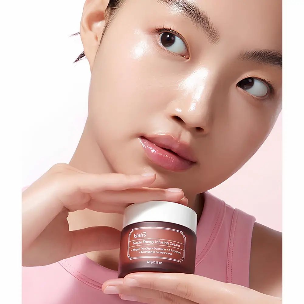 Persona tiene un barattolo di crema marrone con coperchio bianco. Sul barattolo c'è scritto "Maple Energy Infusing Cream".