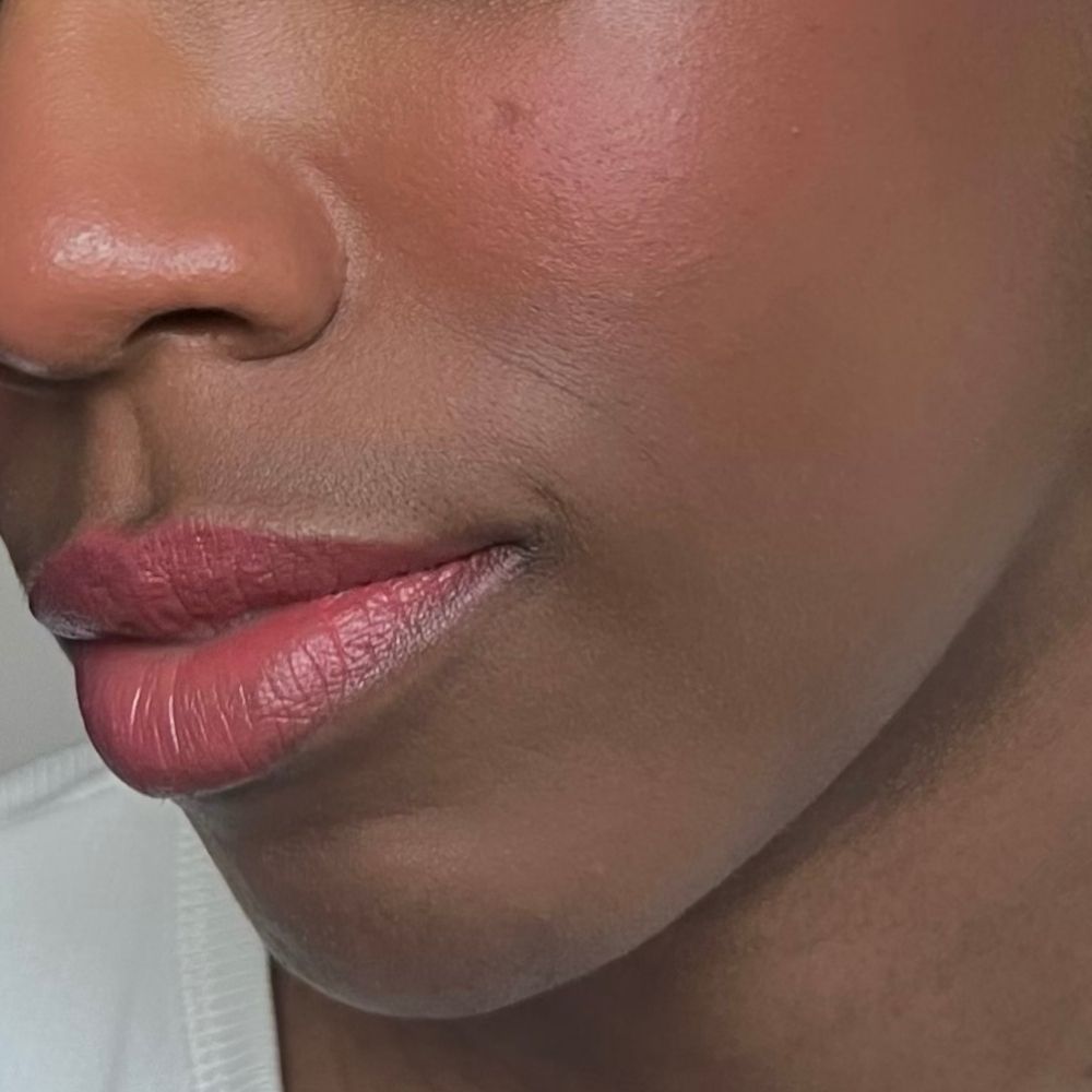 Primo piano di un viso con labbra e guance rosa. Tono della pelle. Rossetto applicato.