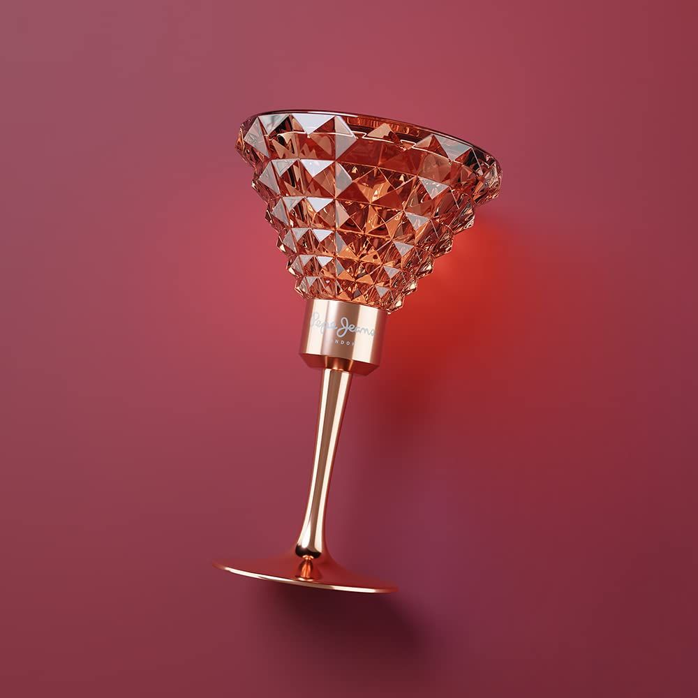 Flacone di profumo a forma di calice. Vetro rosa con motivo geometrico. Stelo e base dorati. Marchio: Pepe Jeans London. Su sfondo rosso.