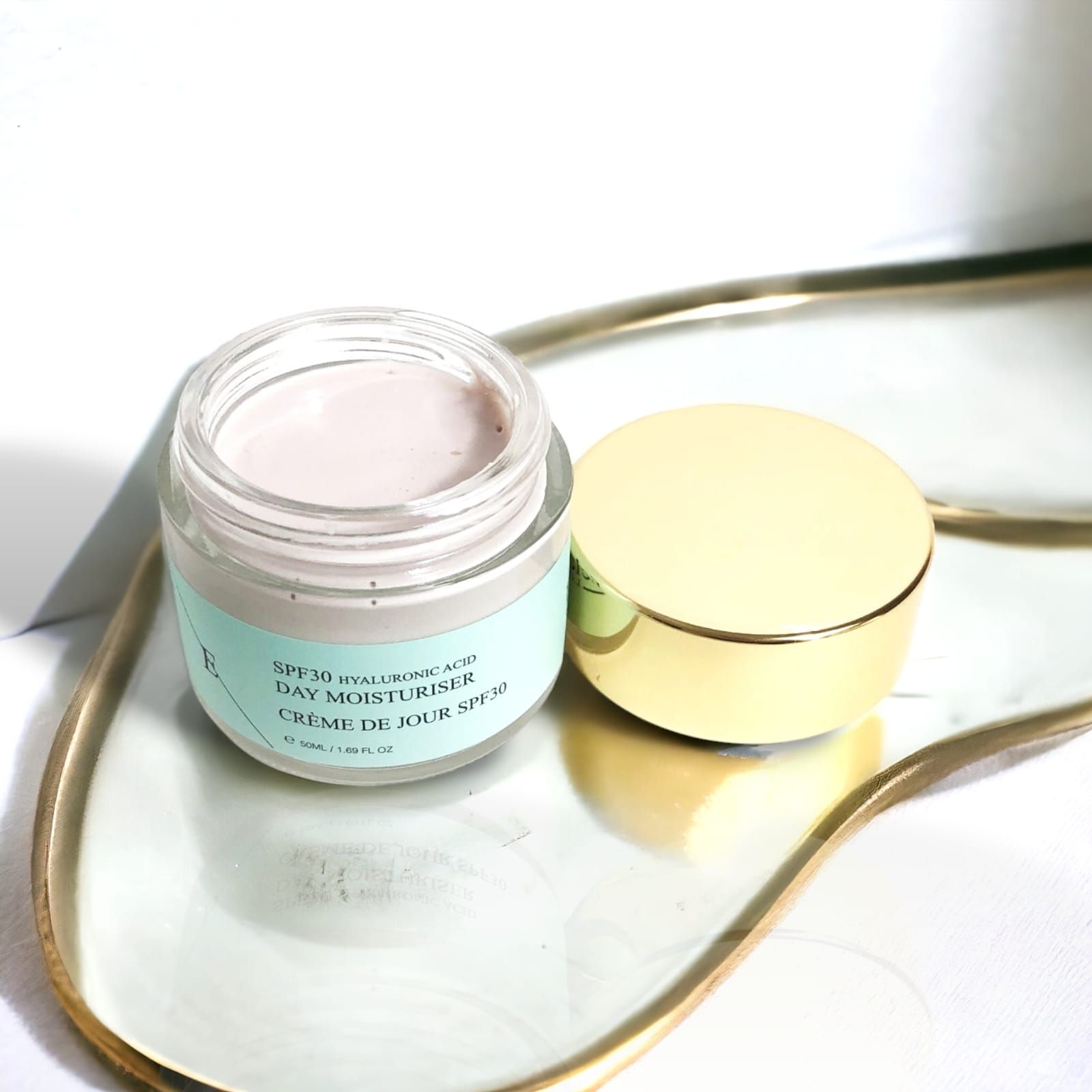 Vasetto di crema giorno con coperchio dorato, aperto, su un vassoio. Scritta: SPF30 Acido Ialuronico Day Moisturiser Crème de Jour SPF30.