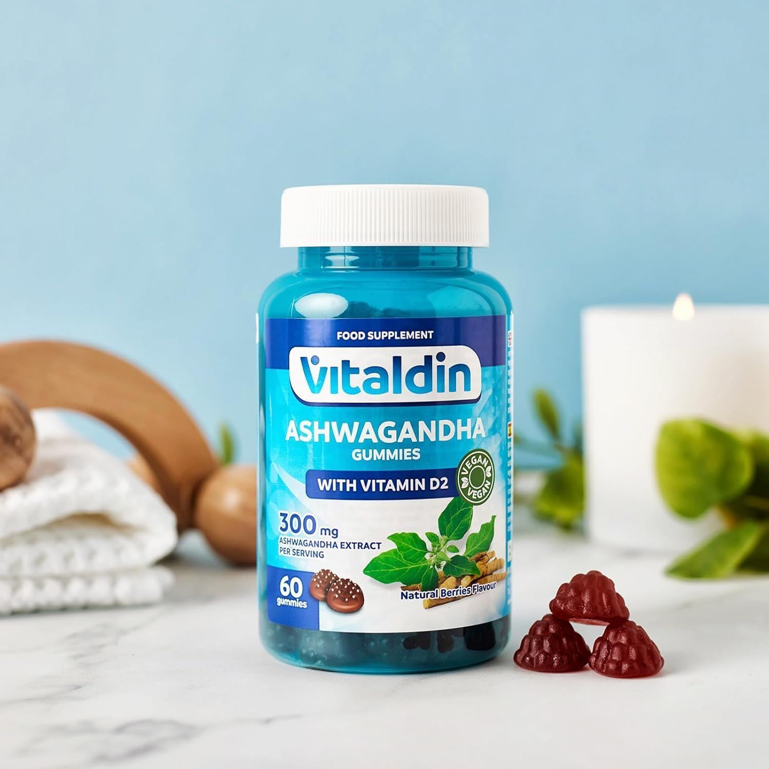 Bottiglia blu VITALDIN Ashwagandha Gummies con coperchio bianco. Accanto ci sono tre caramelle gommose rosse.