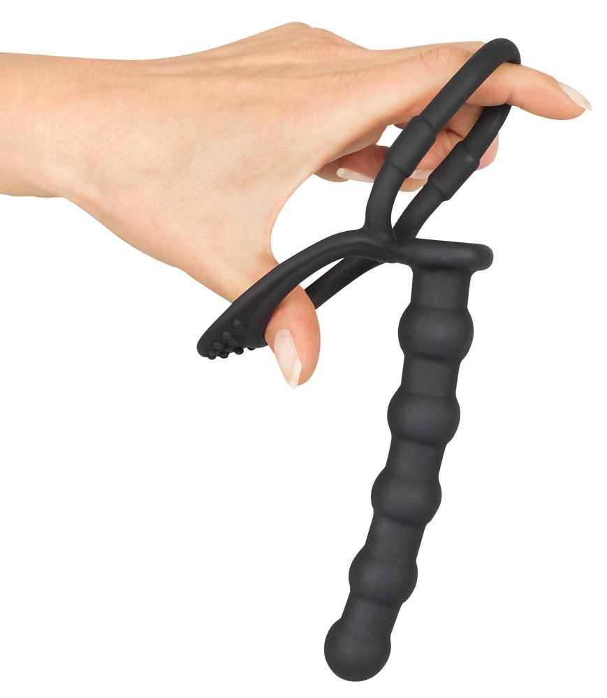 Mano che tiene anello per pene/testicoli nero con dildo anale. Anello con rilievi, dildo scanalato. Silicone.
