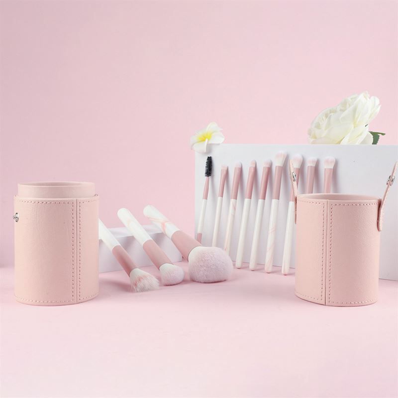 Set di pennelli per trucco con contenitori rosa. Pennelli con manici rosa e bianchi. Varie forme e dimensioni. Posizionati su una superficie rosa.