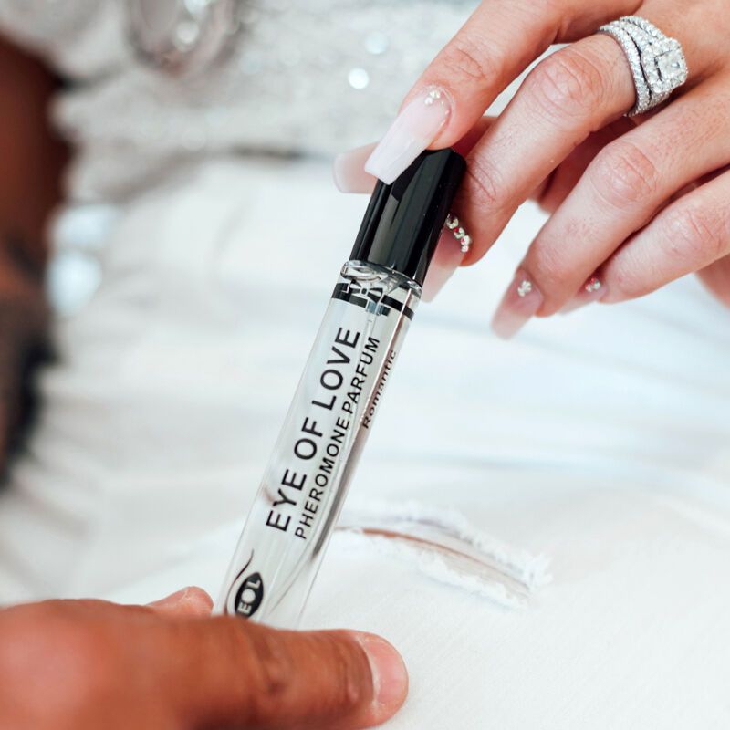 Una mano tiene un flacone di profumo. Scritta: EYE OF LOVE Pheromone Parfum Romantic. Un'altra mano tocca la persona.