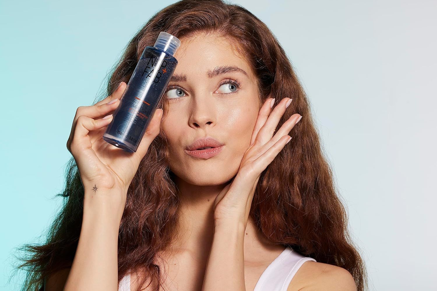 Donna con una bottiglia di Nip+Fab Glycolic Fix Cleanser. Liquido blu, bottiglia trasparente, tappo bianco.